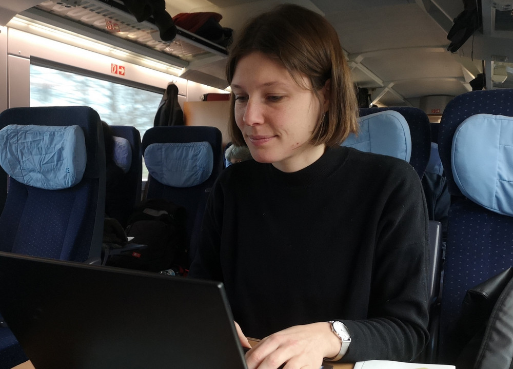 Susanne sitzt im Zug und arbeitet an ihrem Laptop.