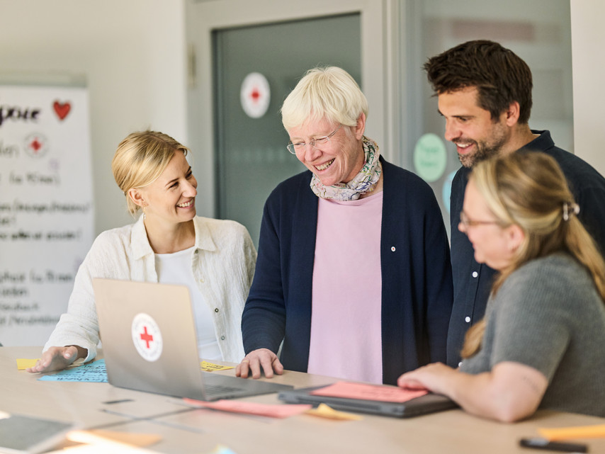 Vier Personen stehen an einem Tisch und schauen auf einen Laptop.