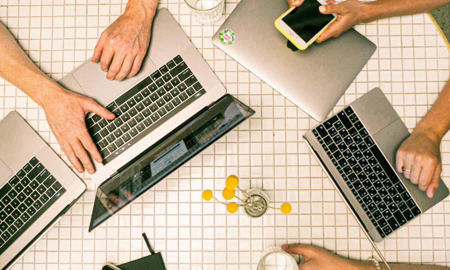 Mehrere Menschenhände, die auf Smartphones oder Laptops gemeinsam arbeiten.