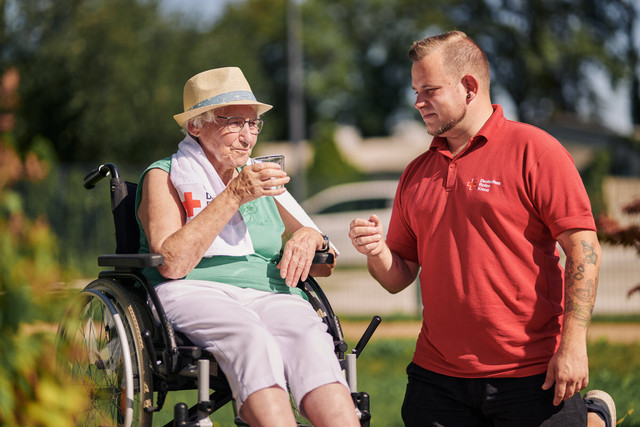 Mitarbeiter des DRK reicht bei Hitze einer Seniorin ein Glas Wasser