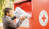 Mann wirft Altkleider in einen Container