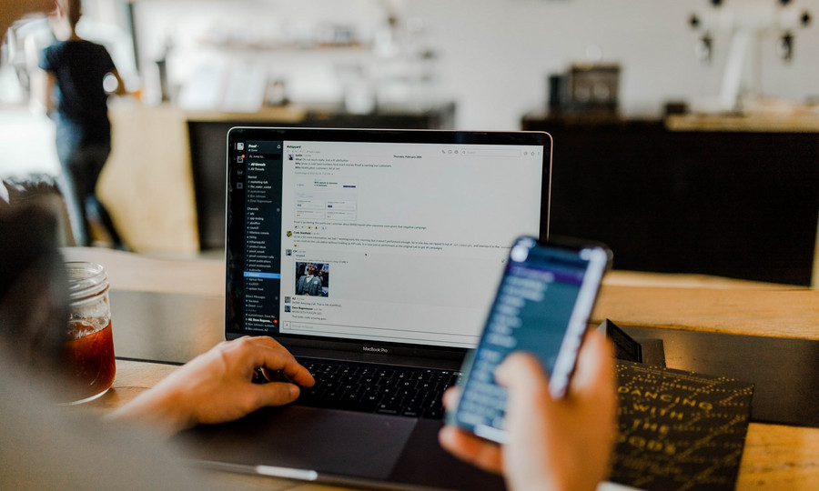 Eine Person nutzt Smartphone vor dem geöffneten Laptop.