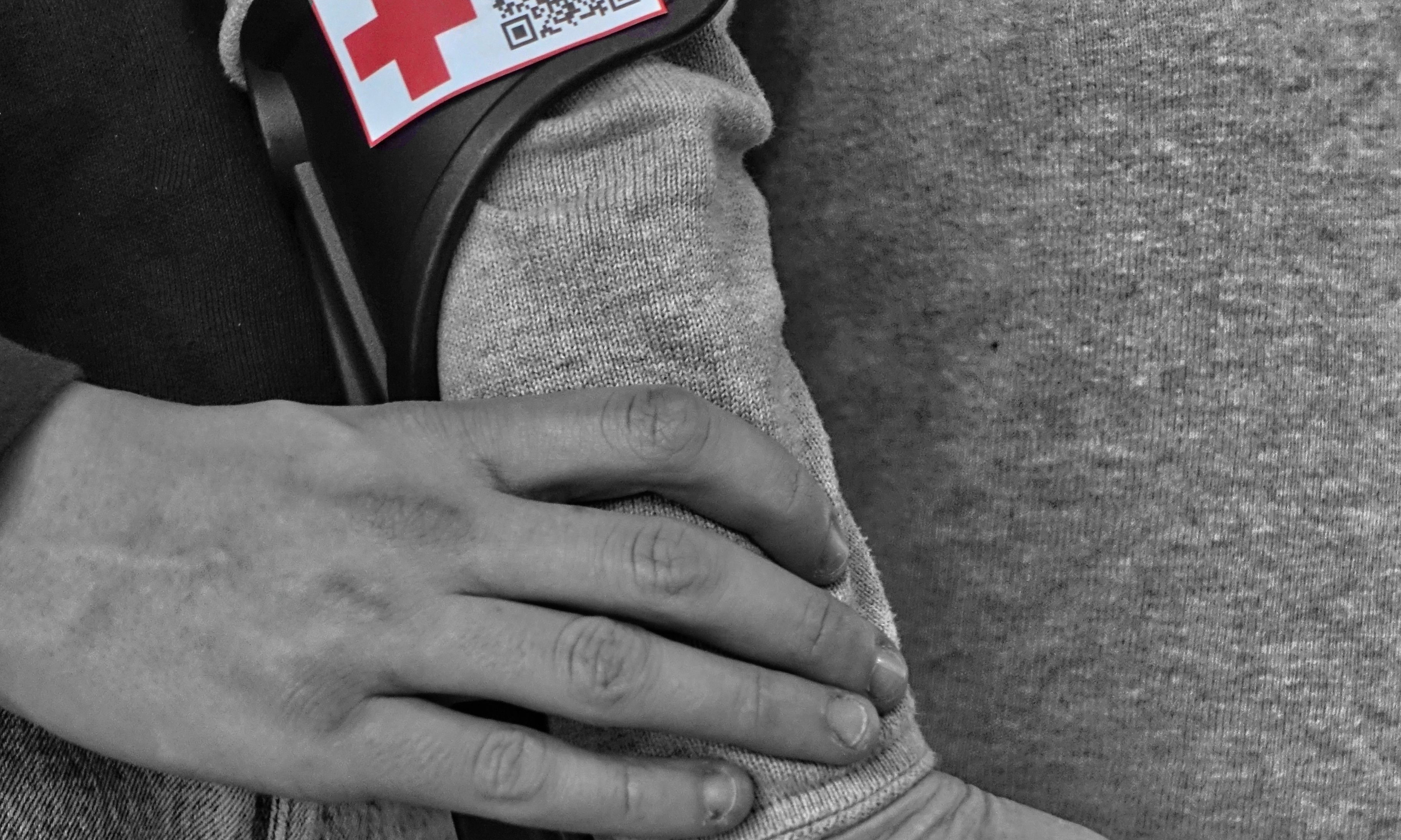 In Schwarz-Weiss eine Person hilft einer weiteren Person, die auf eine Gehstütze geht im Seitenprofil.