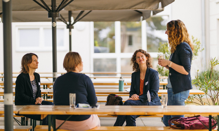 Vier Frauen sprechen an Tischen sitzend miteinander.