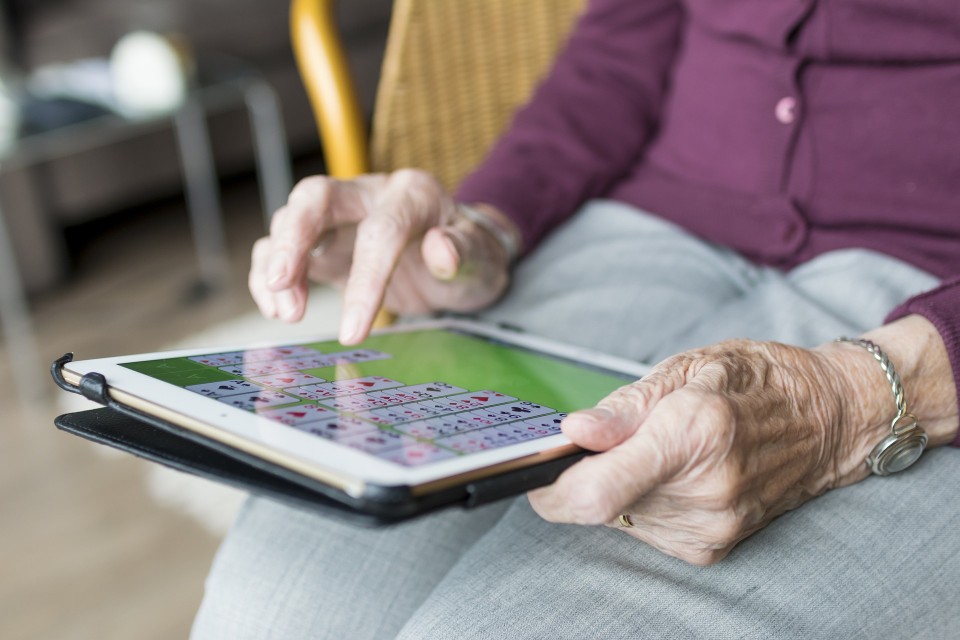 Das Bild zeigt eine Seniorin, die ein Tablet in der Hand hält und darauf ein Spiel spielt.