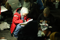 Eine Rotkreuz-Mitarbeiterin hockt auf dem Boden neben einer Frau, die persönliche Dokumente sortiert und notiert etwas auf einem Papier.