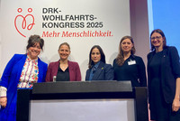 Abbildung der Paneldiskustantinnen vor dem Banner des DRK-Wohlfahrtskongress 2025 mit dem Schriftzug "Mehr Menschlichkeit"