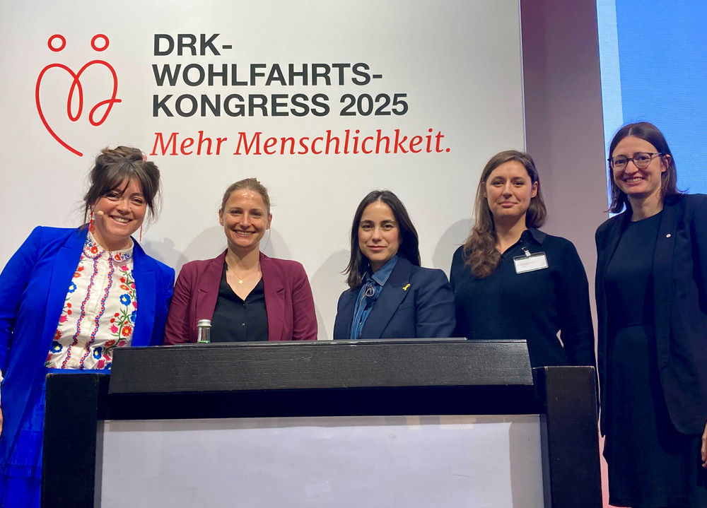Abbildung der Paneldiskustantinnen vor dem Banner des DRK-Wohlfahrtskongress 2025 mit dem Schriftzug "Mehr Menschlichkeit"