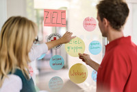 Bild von zwei Personen vor einer gläsernen Wand mit Post-Its.