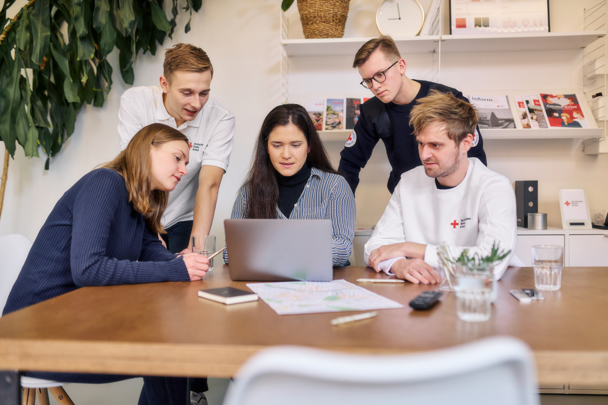 Eine Gruppe von Personen sitzt vor einem Laptop. Sie schauen sich gemeinsam etwas auf dem Gerät an und diskutieren.